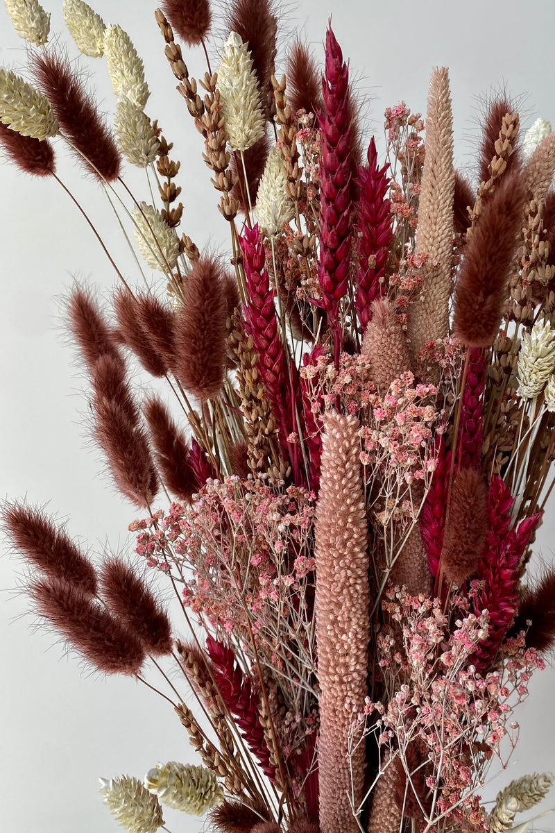 Photo of the Blind Date preserved floral arrangement with pink, mauve and berry colors preserved flowers against a white wall.