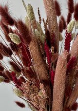 Photo of the Blind Date preserved floral arrangement with pink, mauve and berry colors preserved flowers against a white wall.