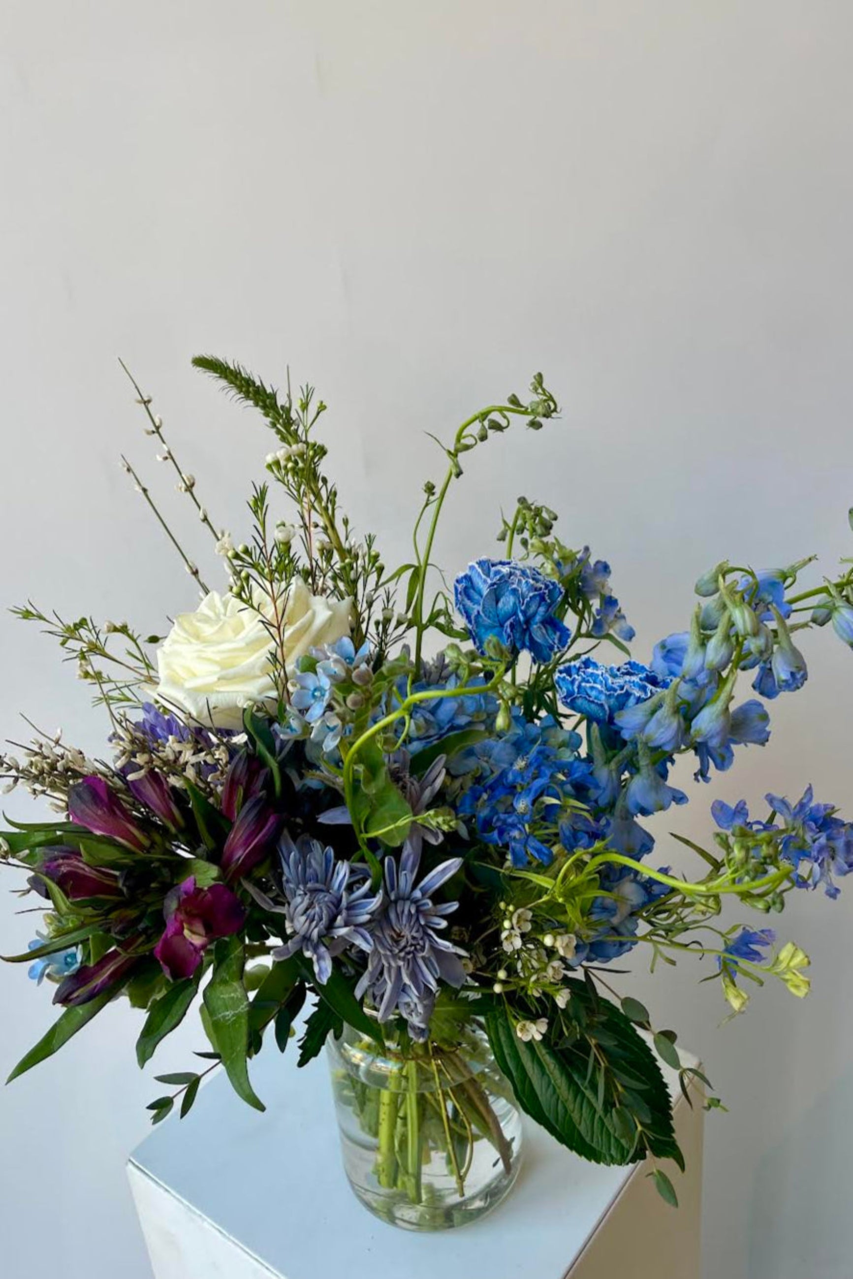 Photo of floral arrangement on a white surface in front of a white wall at Sprout Home. The flowers are various shades of blue, indigo, aqua and teal. ©Sprout Home #size_$100