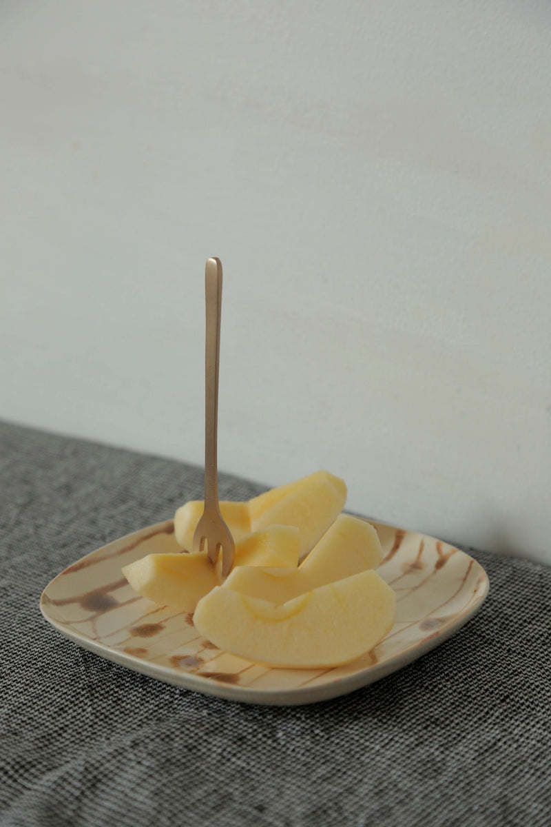 Brass dessert fork by Fog Linen Work stuck in slices of fruit on top of a plate.