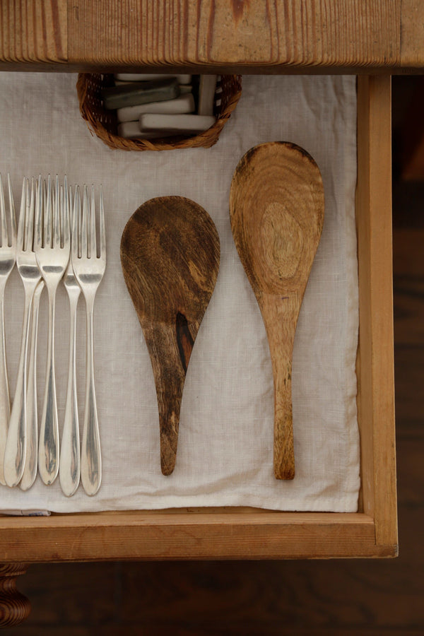 Mango wood spoons by Fog Linen in a drawer next to some silver flatware.