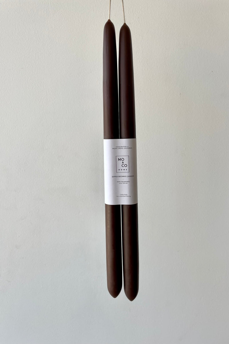 A pair of chestnut brown beeswax taper candles against a white wall.