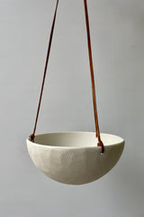 Photot of a porcelain classic hanging planter and leather cord against a white wall.