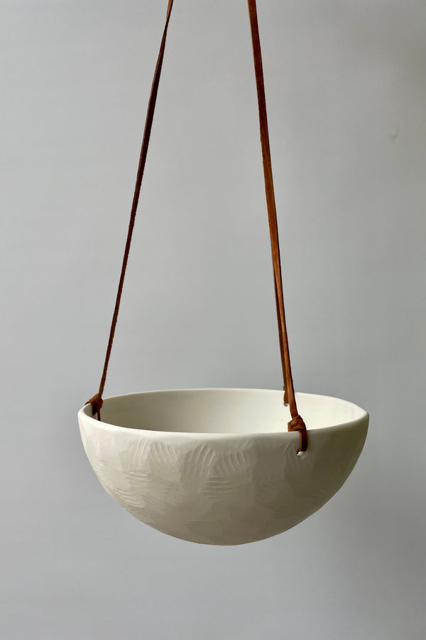 Photot of a porcelain classic hanging planter and leather cord against a white wall.