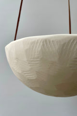 Close photo of detailed texture of a white porcelain classic hanging planter against a white wall.