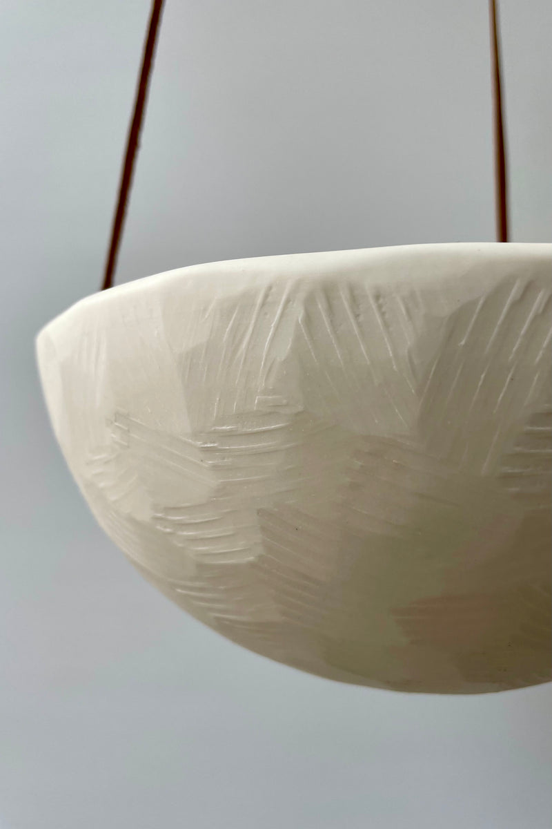 Close photo of detailed texture of a white porcelain classic hanging planter against a white wall.