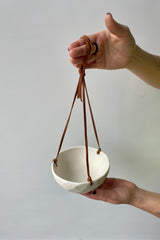 Photo of hands holding a porcelain classic hanging planter against a white wall looking down.