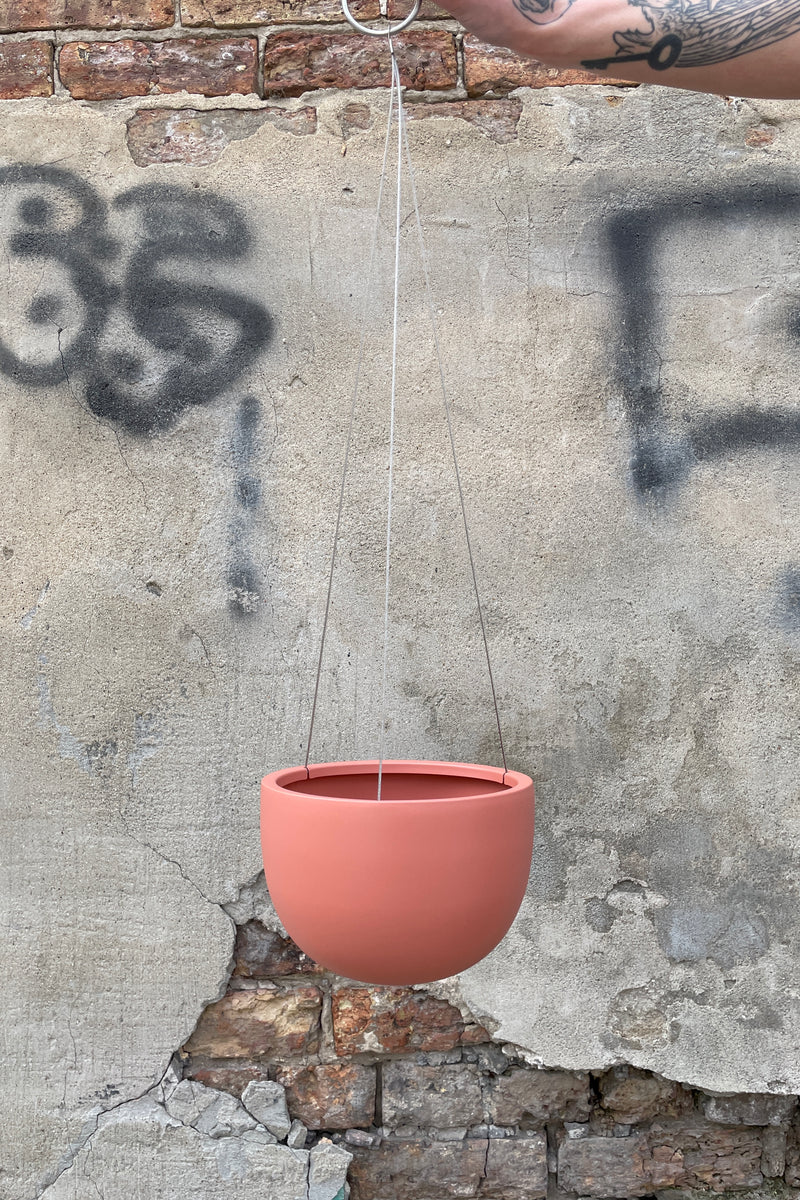Clifton Matte Dusty Pink hanging pot small being held emtpy against a concrete and brick wall. 
