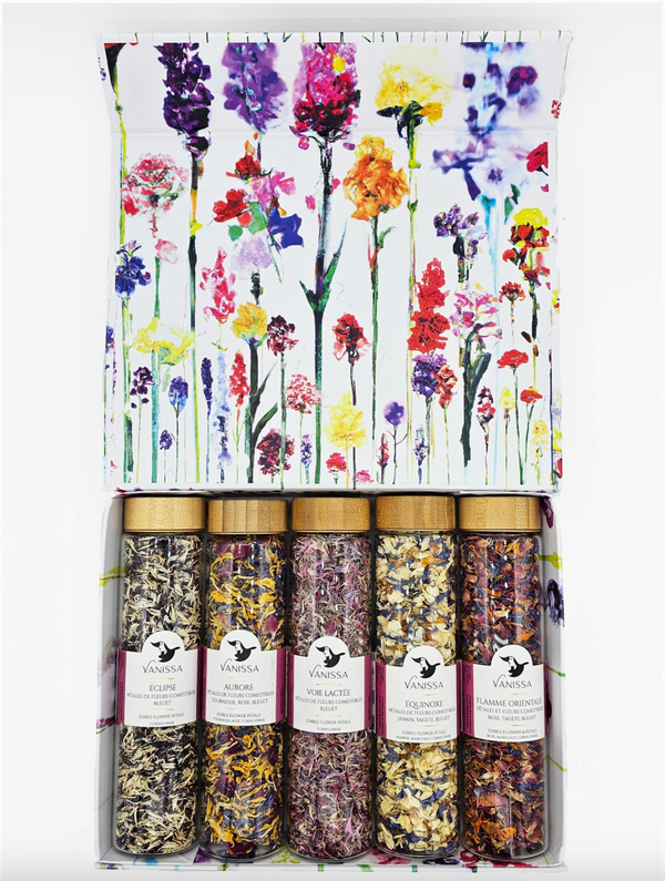 A photo of a white box with colorful floral imagery holding five glass cylinders of colorful flower petals. Shown on a white background.