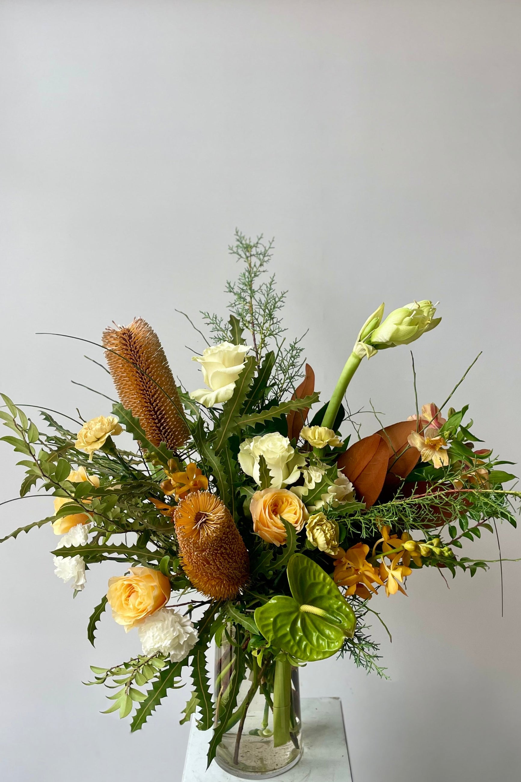 Fresh flowers in a vase in front of a white wall including green foliage, magnolia leaves, roses, amaryllis, banskia and orchids Sprout Home Floral in Chicago ©Sprout Home #size_$200 