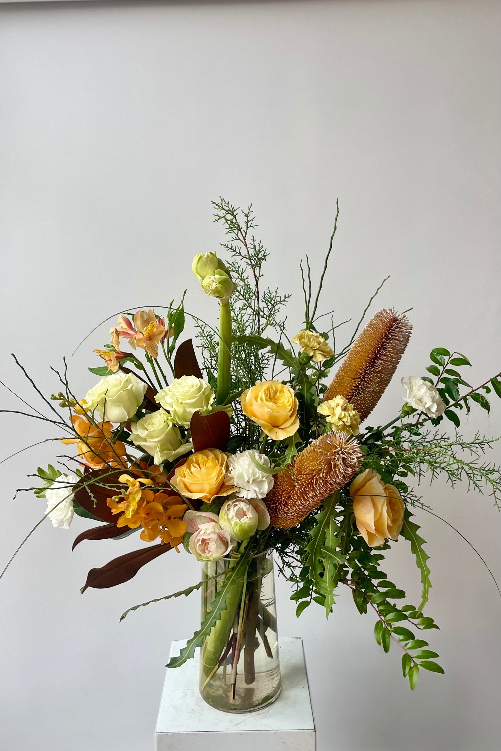 Fresh flowers in a vase in front of a white wall including green foliage, magnolia leaves, roses, amaryllis, banskia and orchids Sprout Home Floral in Chicago ©Sprout Home #size_$200 