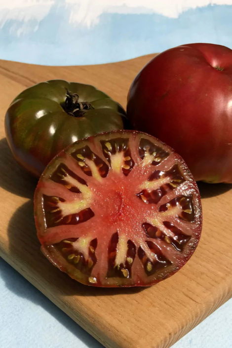 Cherokee Purple tomatoes whole and sliced n a wood board by Hudson Valley Seed Company.