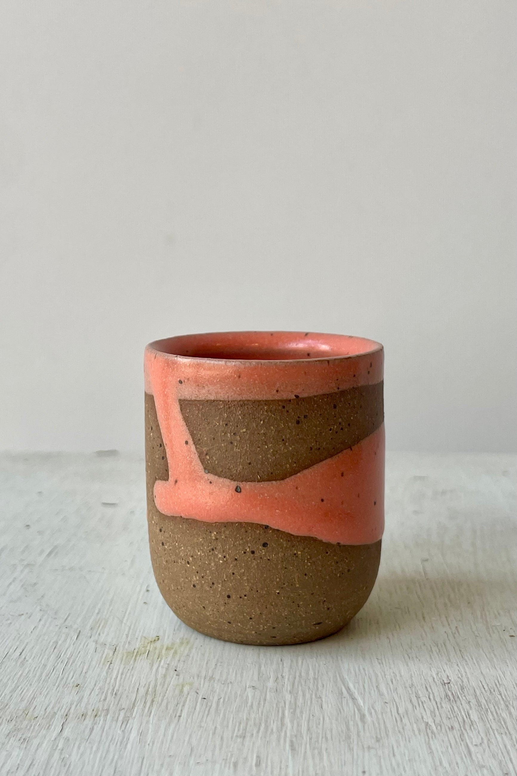 Photo of a small cup with brown clay and a coral glaze in front of a white wall ©Sprout Home
