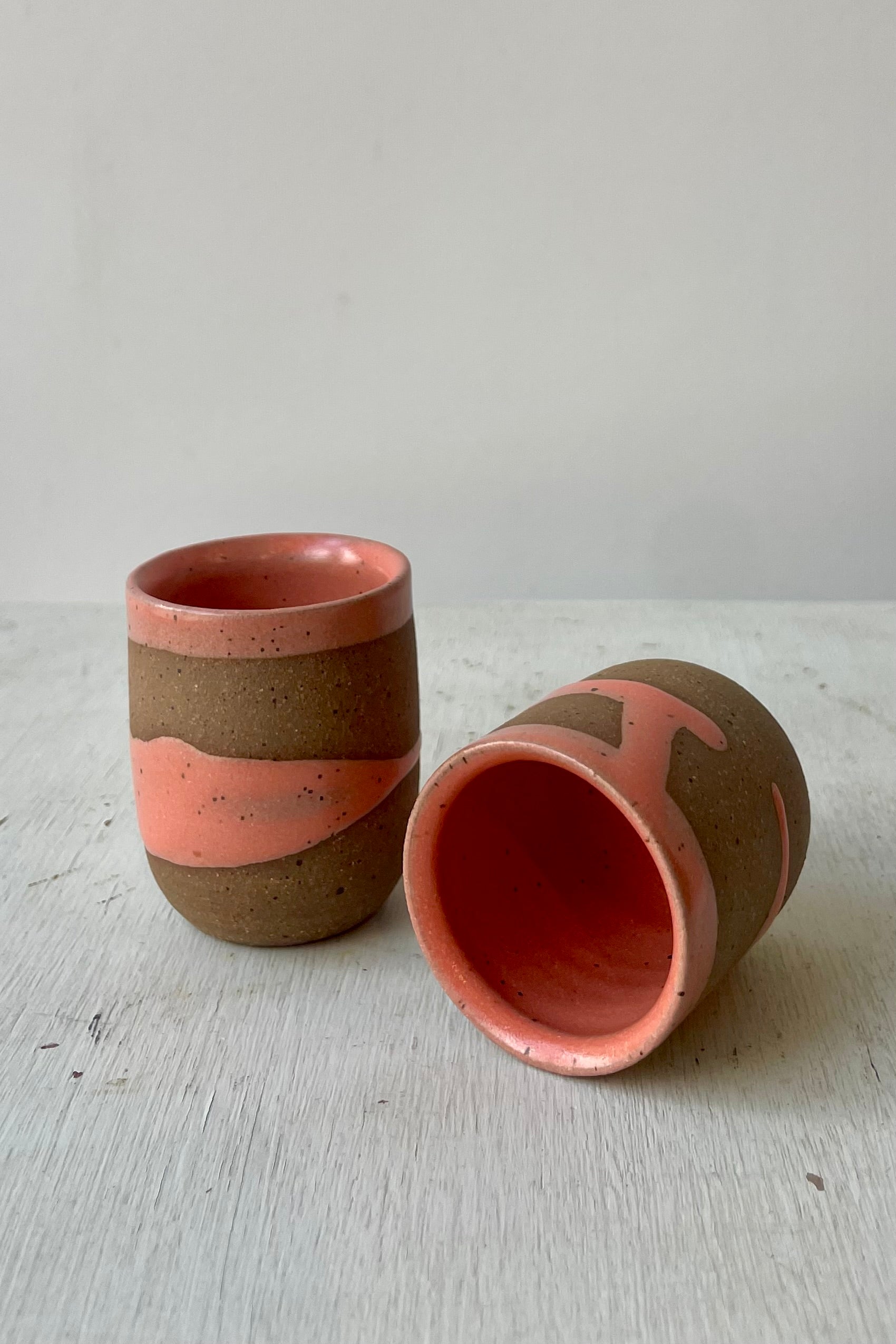 Photo of a pair of small cups with brown clay and a coral glaze in front of a white wall ©Sprout Home