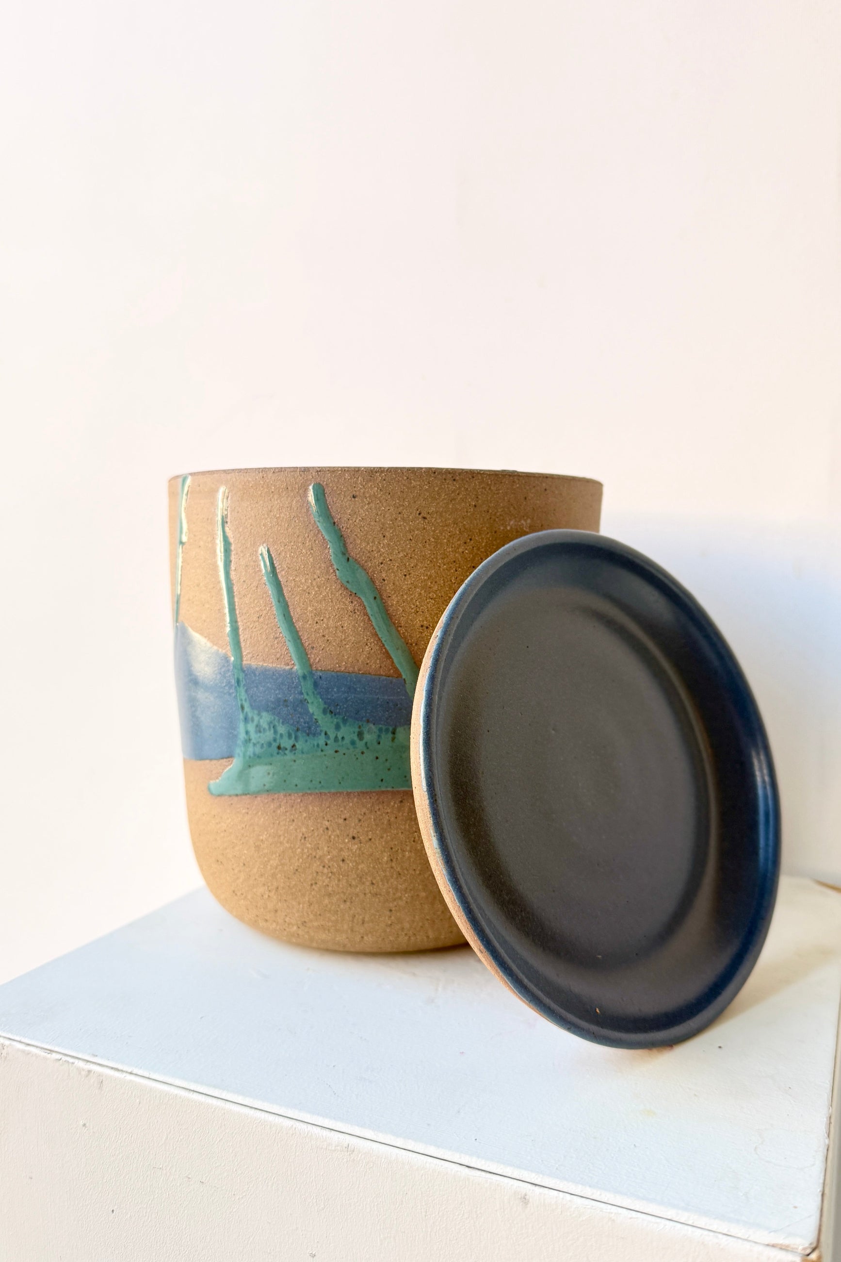 Cylinder Pot & Saucer Denim and Dark Teal Splash Glaze 6.5" with its saucer leaning against it on a light surface ©Sprout Home