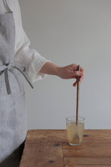 Mango wood muddler by Fog Linen Work being stirred in a drink and held in hand by a person in an apron