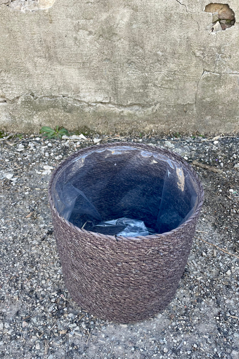 Photo from above of black seagrass basket with liner against a cement wall.