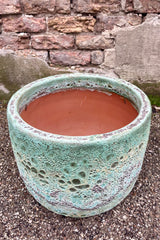 Photo of a Large Coarse Volcano Glaze pot with a heavily textured glaze. Shown outdoors on a paved surface against a brick wall. Shown from above.