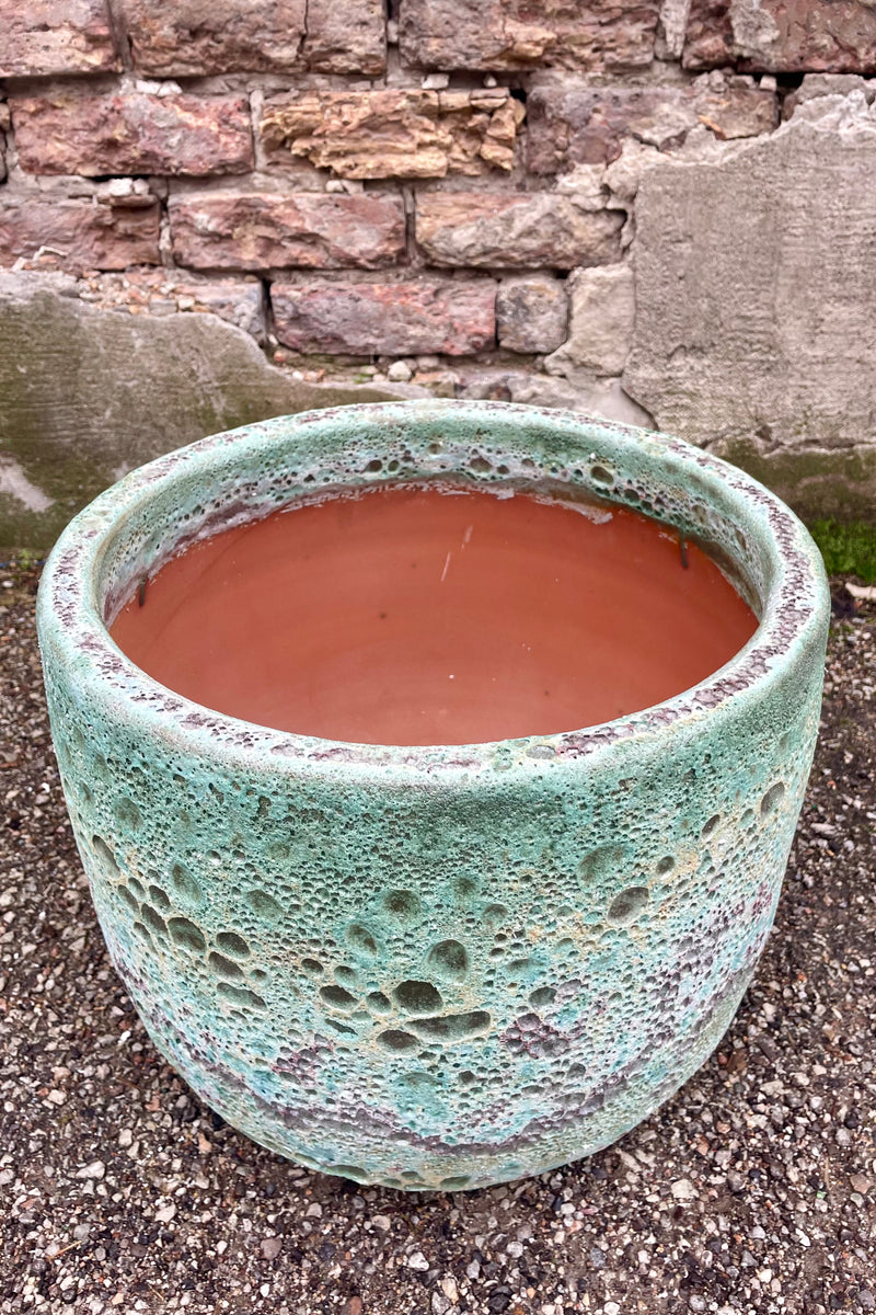 Photo of a Large Coarse Volcano Glaze pot with a heavily textured glaze. Shown outdoors on a paved surface against a brick wall. Shown from above.