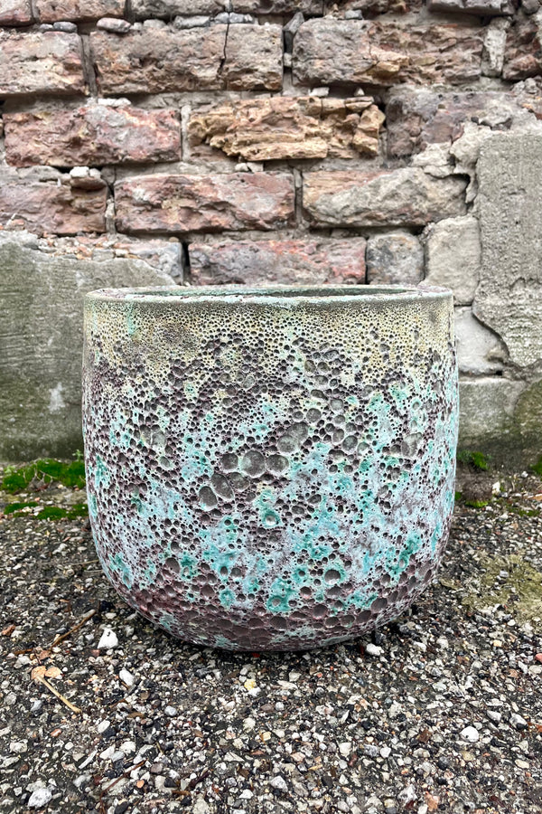 Photo of a Medium Coarse Volcano Glaze pot with a heavily textured glaze. Shown outdoors on a paved surface against a brick wall. Shown from the side.