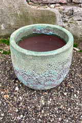 Photo of a Small Coarse Volcano Glaze pot with a heavily textured glaze. Shown outdoors on a paved surface against a brick wall. Shown from above.