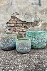 Photo of a trio of three sizes of Coarse Volcano finish pottery, shown on a paved surface against a brick wall.