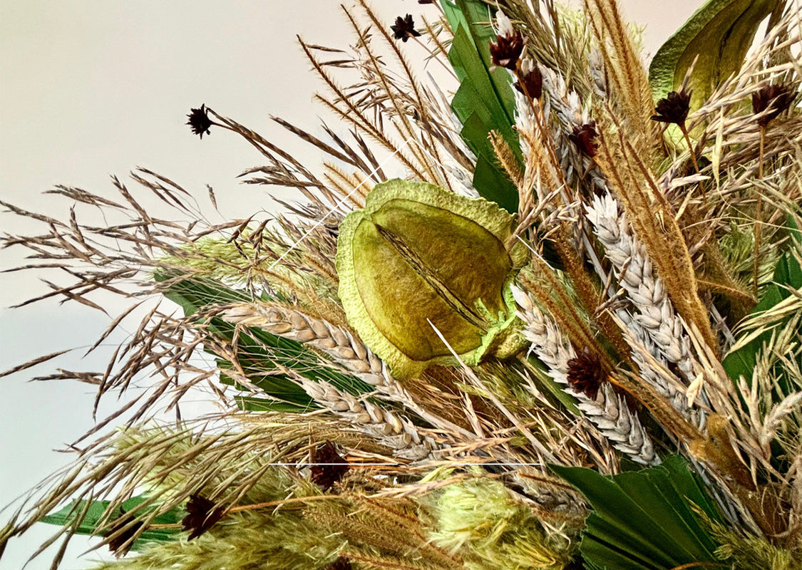 Dried floral arrangement with green, gold and beige foliage against a white wall