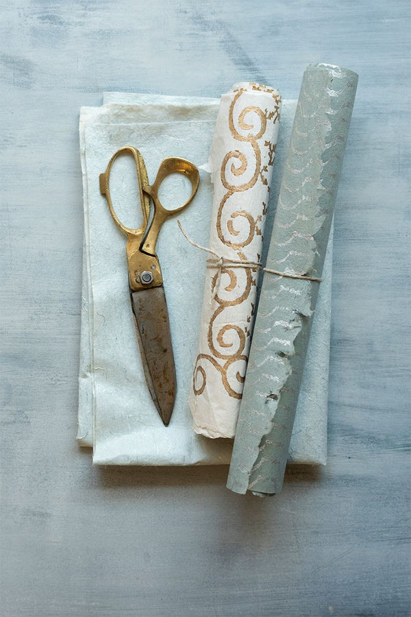 Brass and steel scissors on a folded paper with rolls of art paper next to it.  