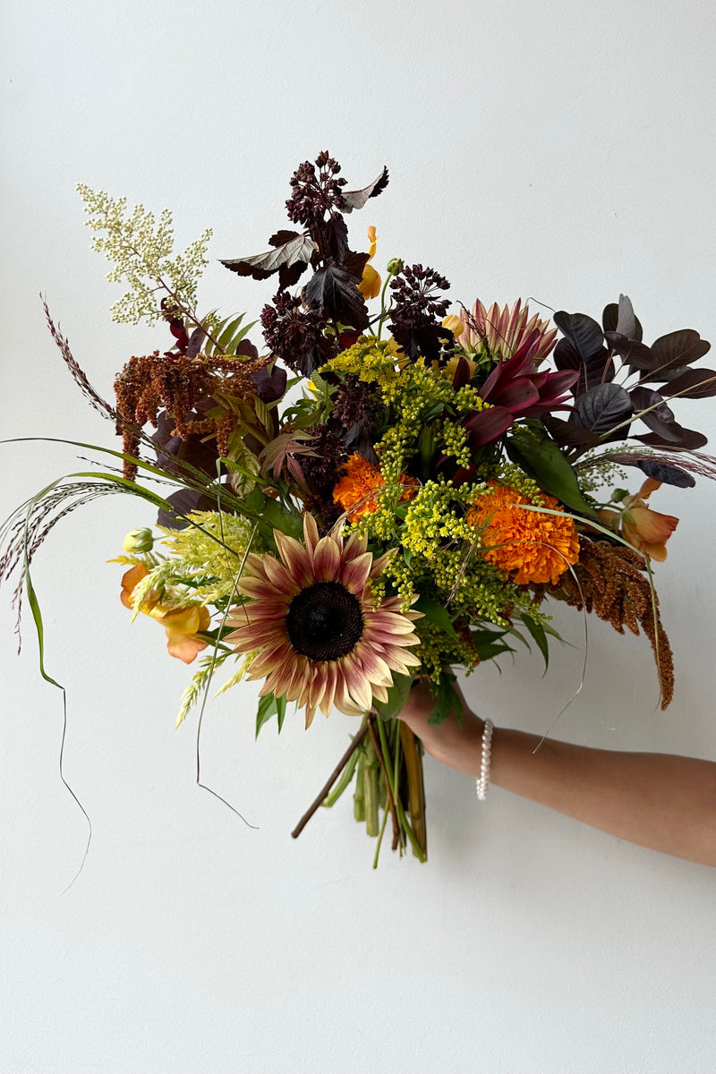 Sprout Home 'Earth' arrangement featuring a sunflower in July being held against a white wall. 