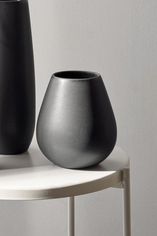 The black iron Ease vase on a white table sitting next to a taller vase off to the side.