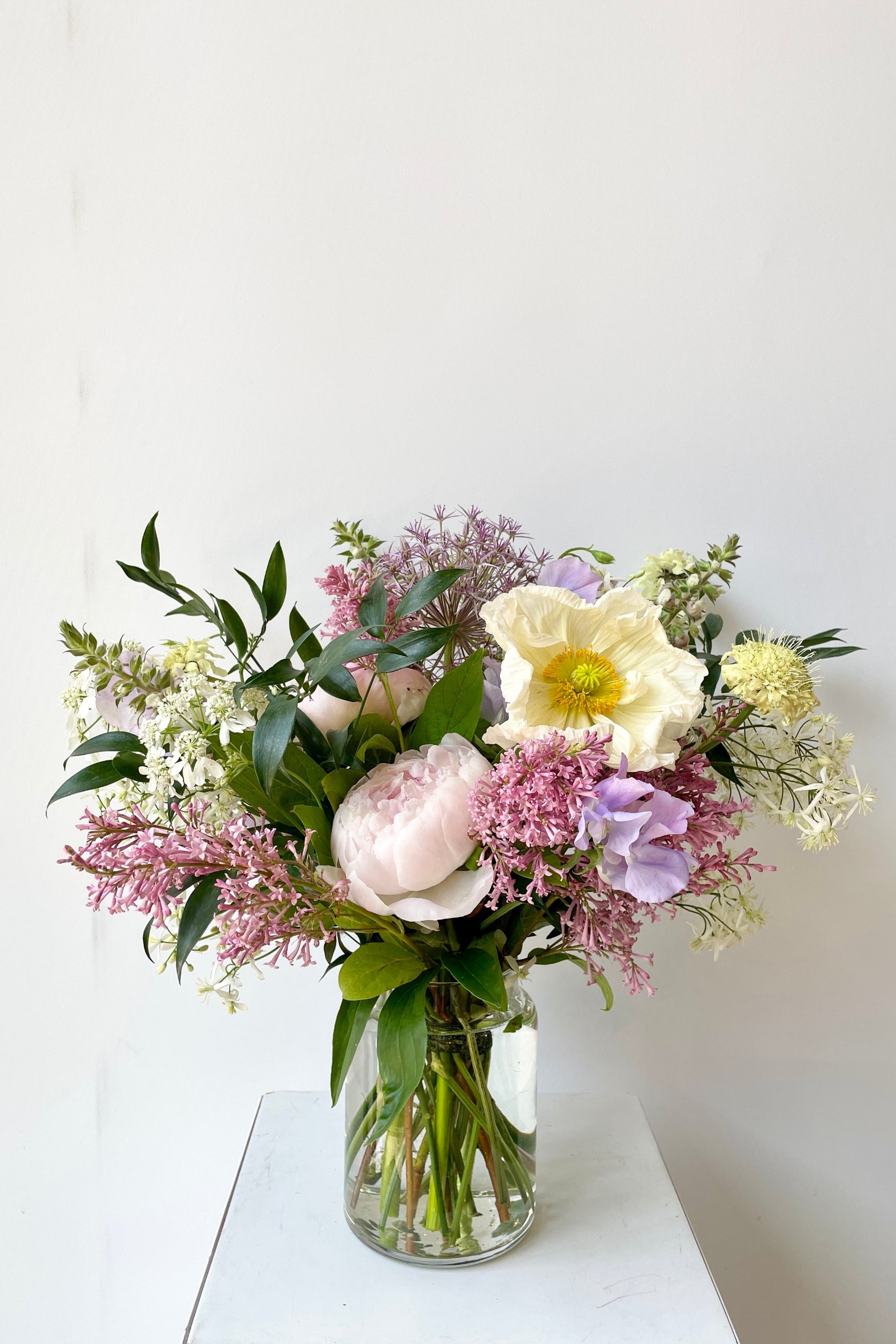 A dawn arrangement featuring a white poppy and light purple pink lilac the end of May in a Libbey jar by Sprout Home. ©Sprout Home #size_$75