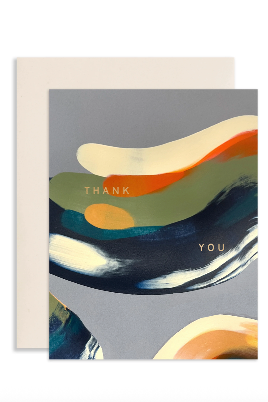 A greeting card with an abstract design of dark various colors on a gray background with an embossed Thank You message. Shown in front of a white wall. ©Sprout Home