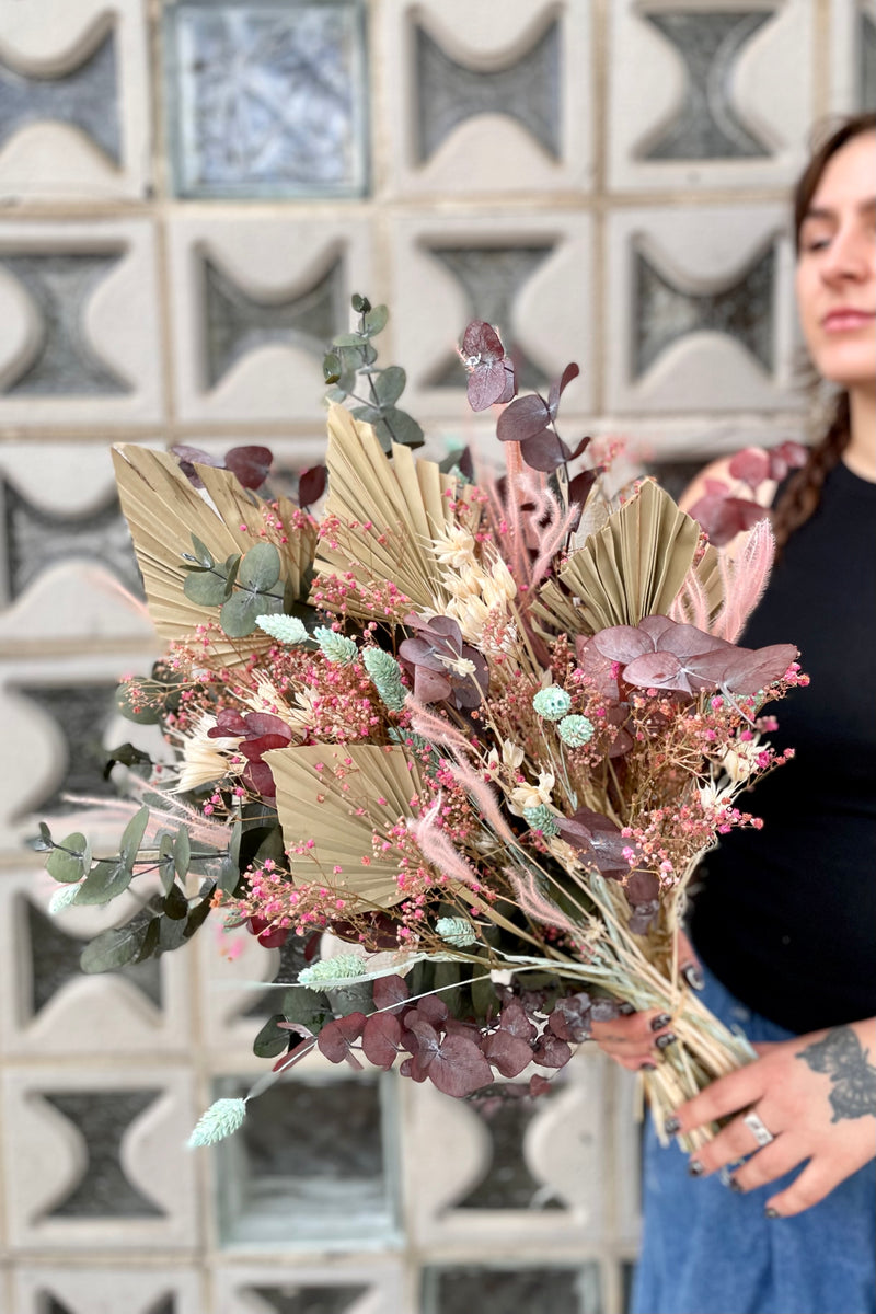 'Faerie' preserved floral arrangement by Sprout Home being held by one of our associates in front of glass block. 