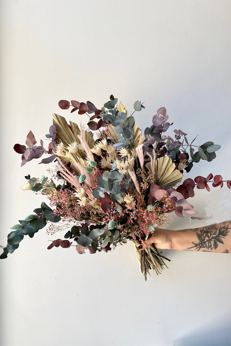 'Faerie' preserved floral arrangement created by Sprout Home being held against a white wall. 