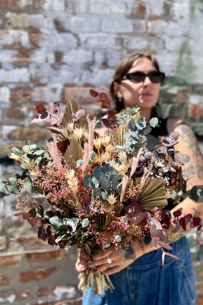 custom Sprout Home preserved floral arrangement called 'Faerie' being held in front of a graffiti wall by a Sprout Home associate