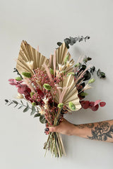 'Faerie' dried floral arrangement by Sprout Home being held against a white wall showing off its neutral and pastel palette.