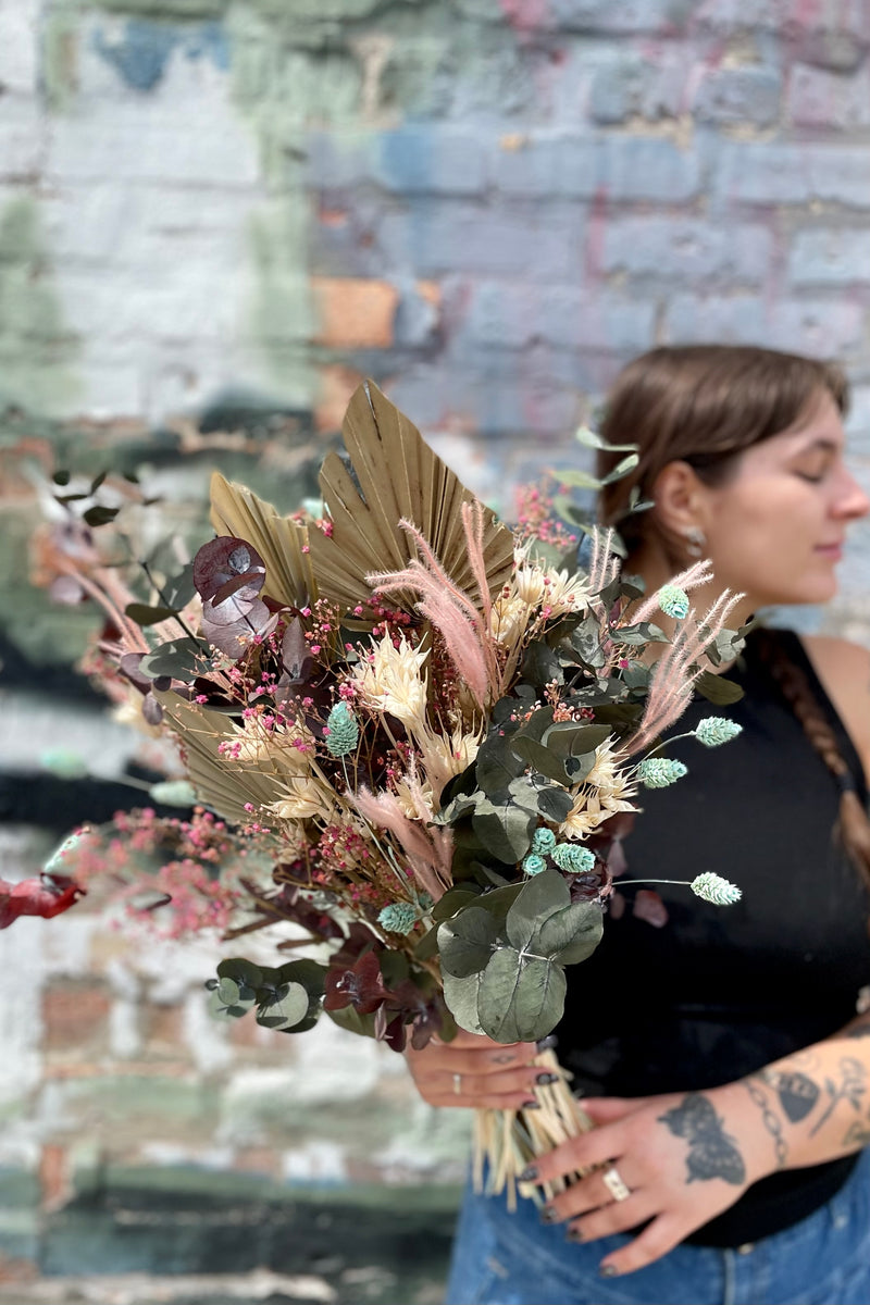 'Faerie' arrangement by Sprout Home being held by a Sprout Home florist in front of a graffiti wall. 