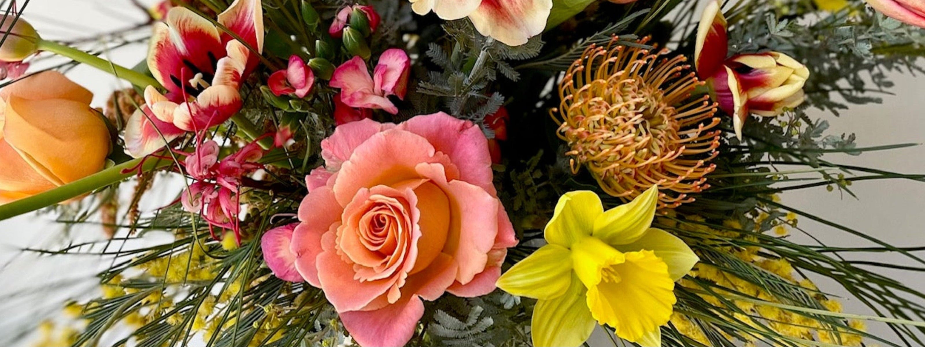 Colorful bouquet of flowers including roses and daffodils on a light background ©Sprout Home