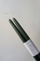 Close photo of forest green beeswax taper candles against a white wall.