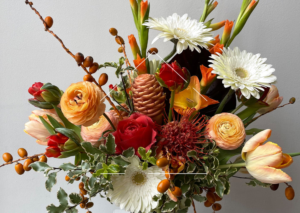 Fresh floral arrangement with red, orange and white flowers against white wall