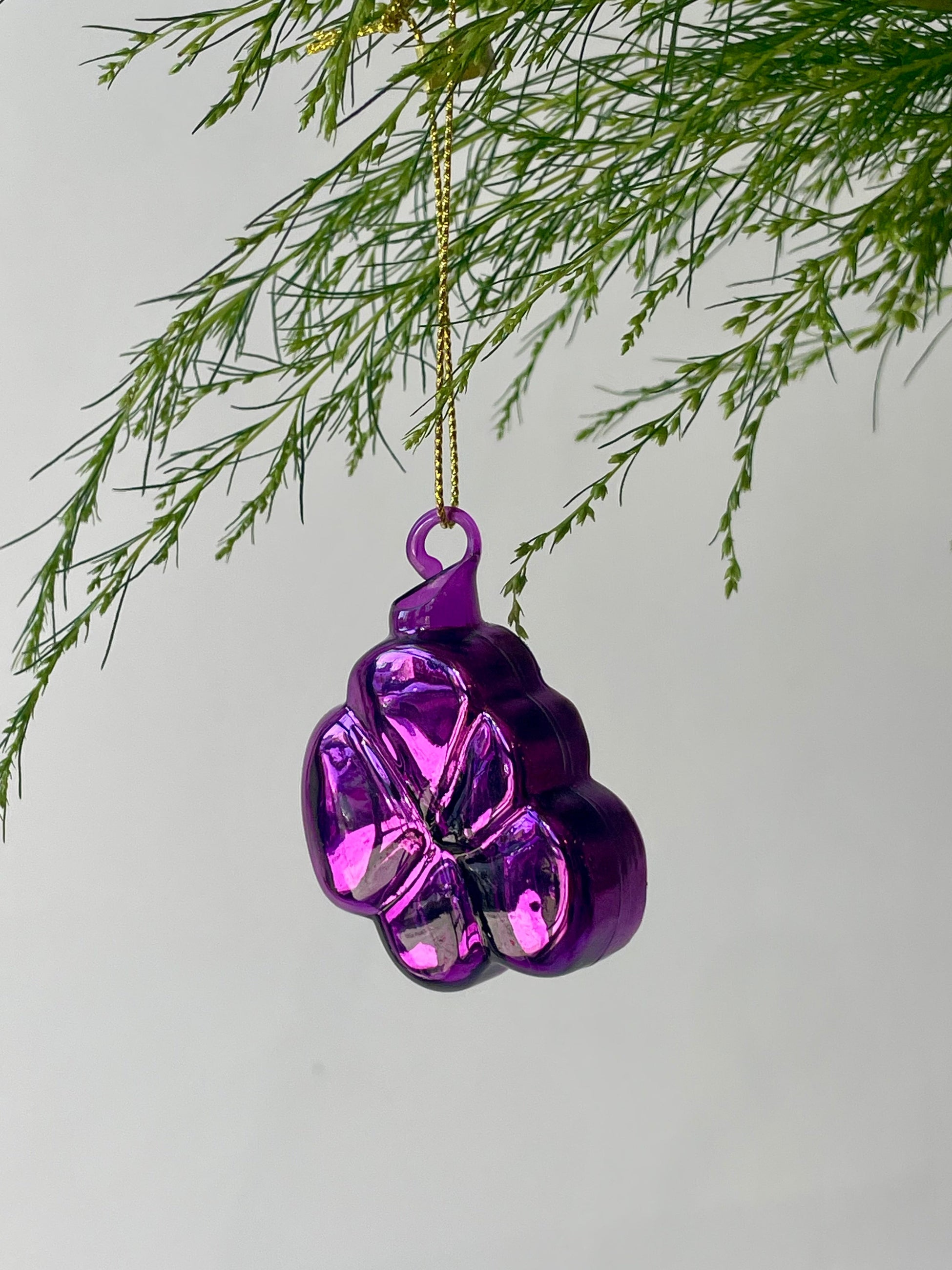 A purple floral ornament shaped like a violet with glitter hangs from a branch in front of a gray wall ©Sprout Home