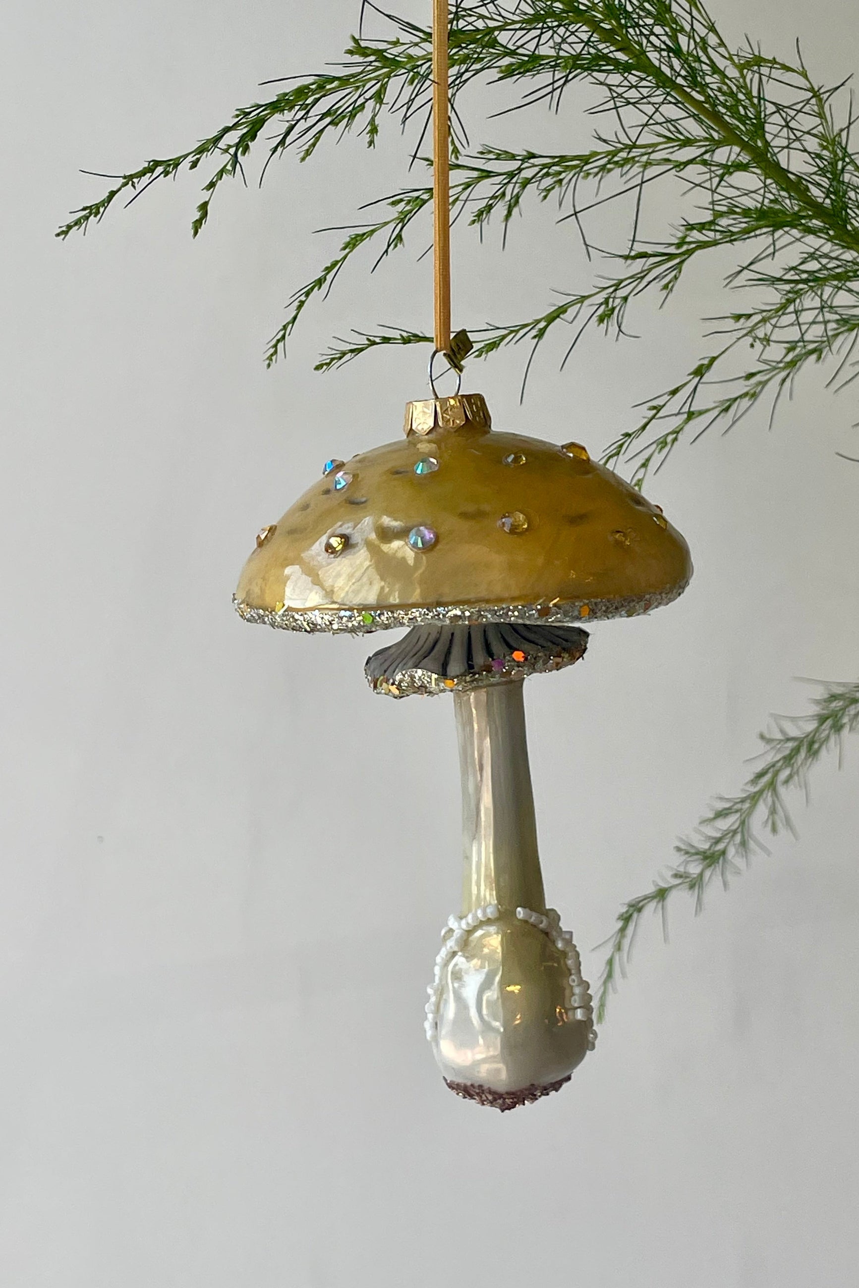 Photo of a yellow mushroom ornament with glitter hanging from a branch in front of a white wall ©Sprout Home