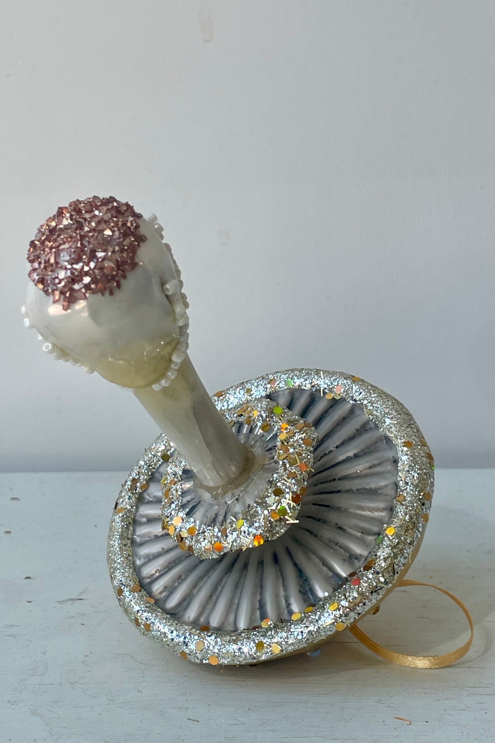 Photo of the underside of a glittery ornament shaped like a yellow mushroom in front of a white wall ©Sprout Home