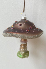 The purple wooded glen mushroom ornament being held against a white wall  available at Sprout Home. 