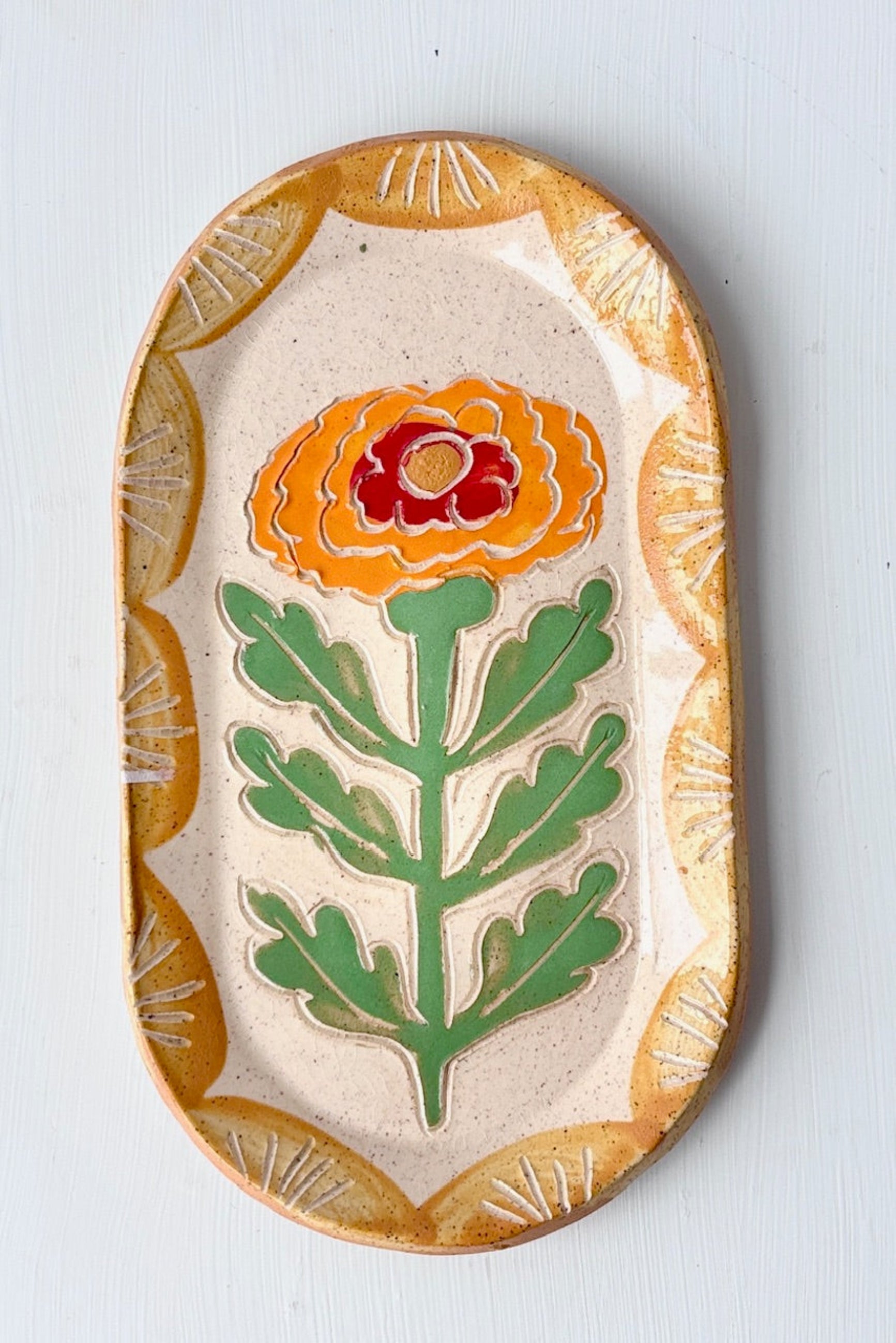 Decorative Goldie Marigold ceramic plate with sgraffito floral design against a white background ©Sprout Home