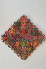 Photo of a colorful patchwork Daisy pattern Abaca placement against a white wall.