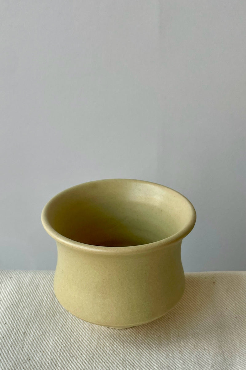 Photo of Little Fire Ceramics hourglass cup with butter glaze shown from the above. The cup sits on a white cloth against a white wall.