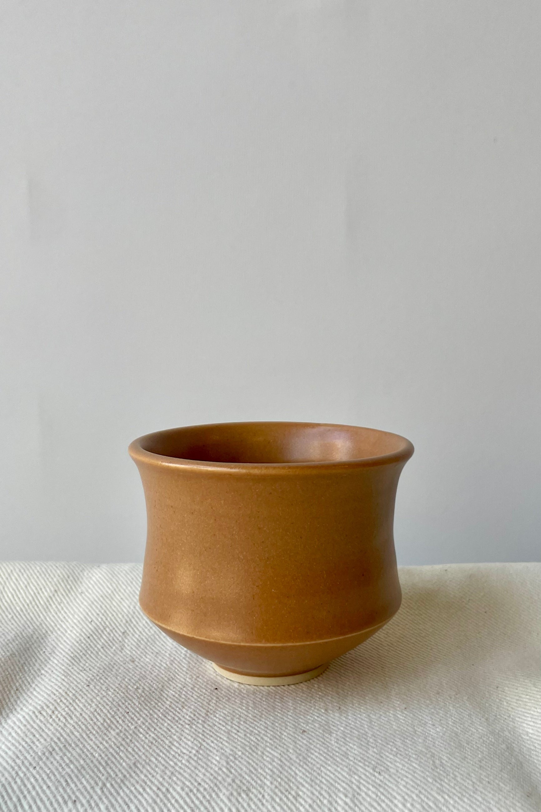Photo of Little Fire Ceramics Hourglass cup with a camel glaze on a white surface ahead of a white wall. ©Sprout Home
