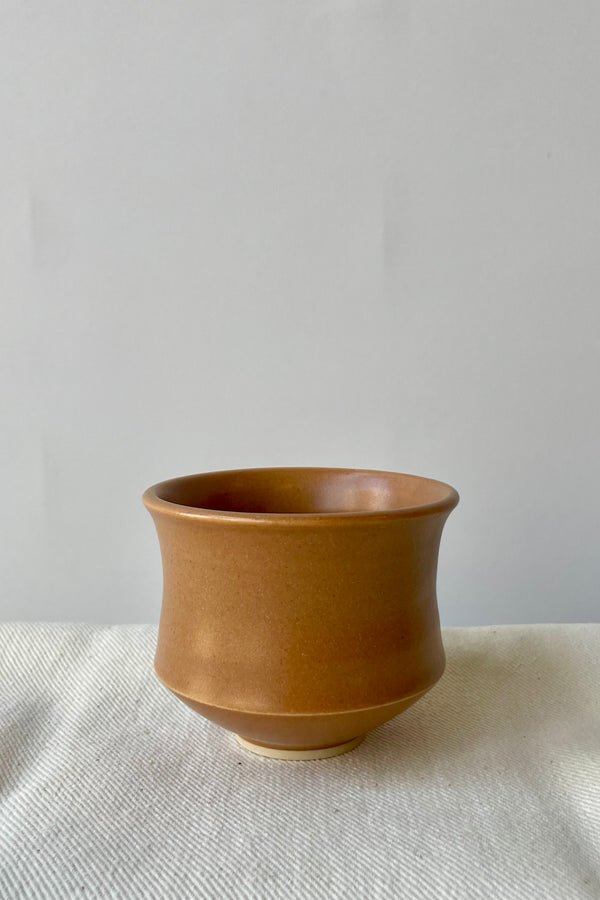 Photo of Little Fire Ceramics Hourglass cup with a camel glaze on a white surface ahead of a white wall.