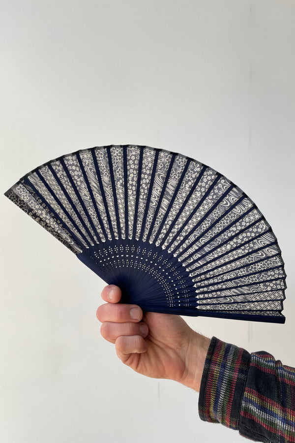 A blue swirl pattern fan with blue bamboo being held in hand against a white backdrop. 
